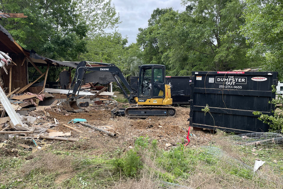 A container beside an excavator taking down an outbuilding