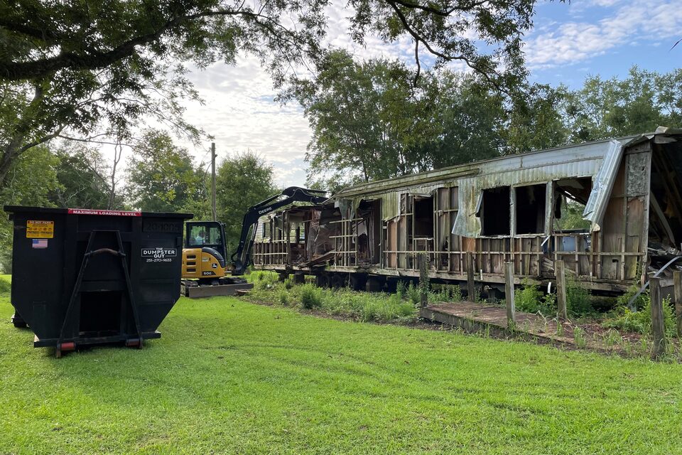 A container on the grass while a mobile home is torn out behind it