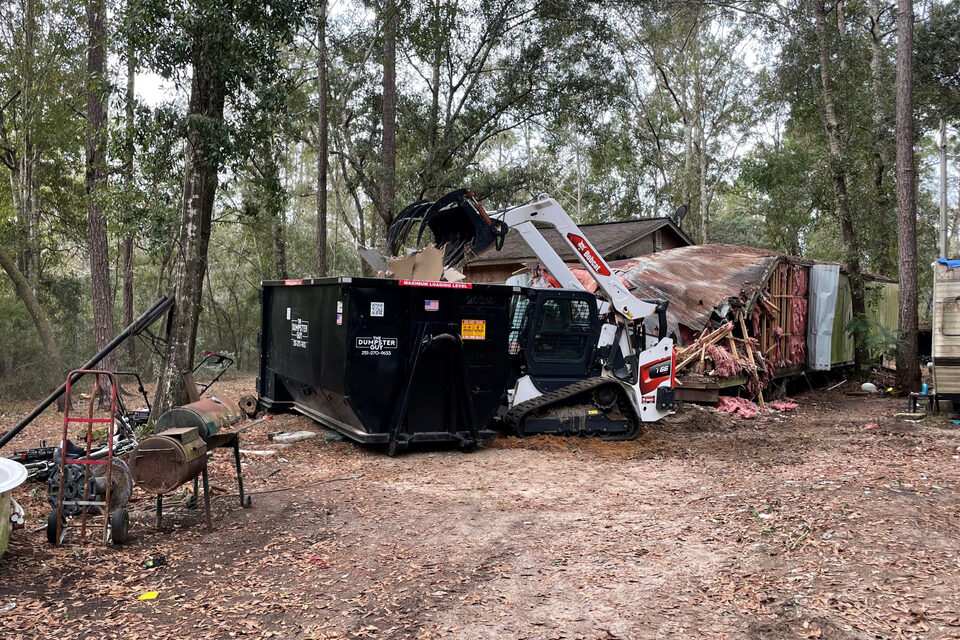 A container on a cleared wooded lot during a property cleanout